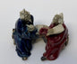 Ceramic Figurine Two Men Sitting On A Bench Holding Fan & Pipe- 2.0" Color: Red & Blue